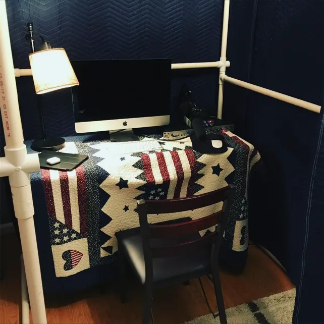 Inside the packing-blanket booth at night, with a lamp, computer and microphone
